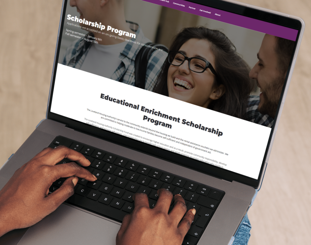A person types on a laptop displaying a website about a Scholarship Program, featuring a banner with smiling students and text about the Educational Enrichment Scholarship Program.