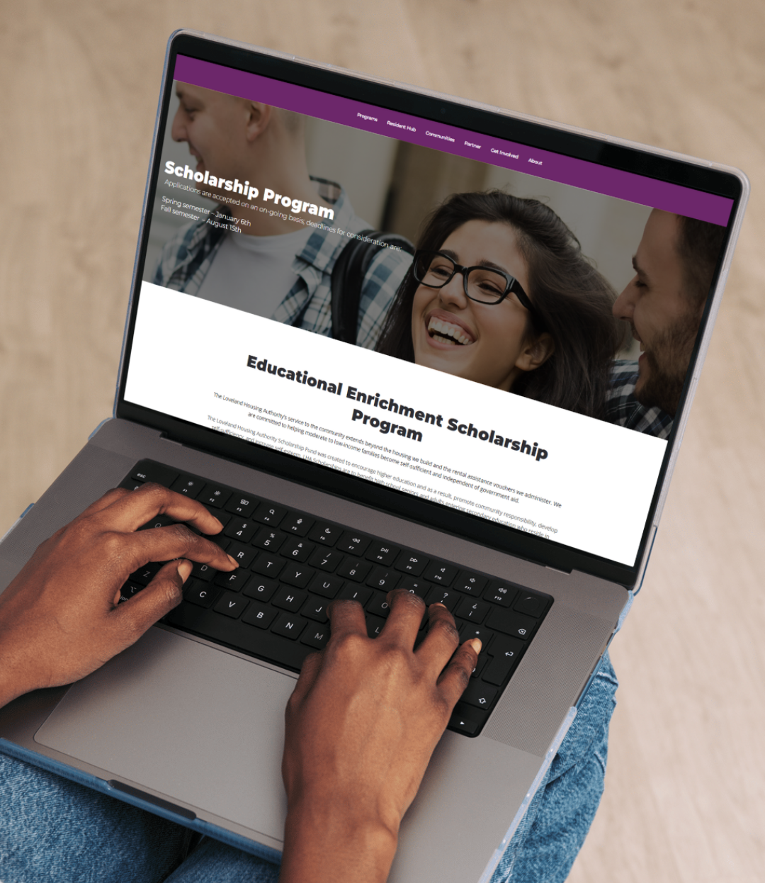 A person types on a laptop displaying a website about a Scholarship Program, featuring a banner with smiling students and text about the Educational Enrichment Scholarship Program.